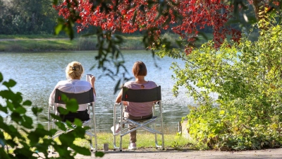 Zwei Frauen sitzen im baden-württembergischen Ertingen an einem See in der Sonne. (Foto: Thomas Warnack/dpa)