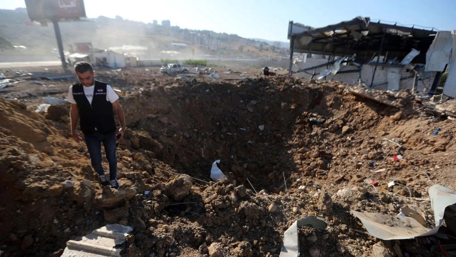 Ein libanesischer Polizist steht in der Nähe eines Kraters nach einem israelischen Luftangriff auf einen Hangar im Südlibanon. (Foto: Mohammed Zaatari/AP/dpa)