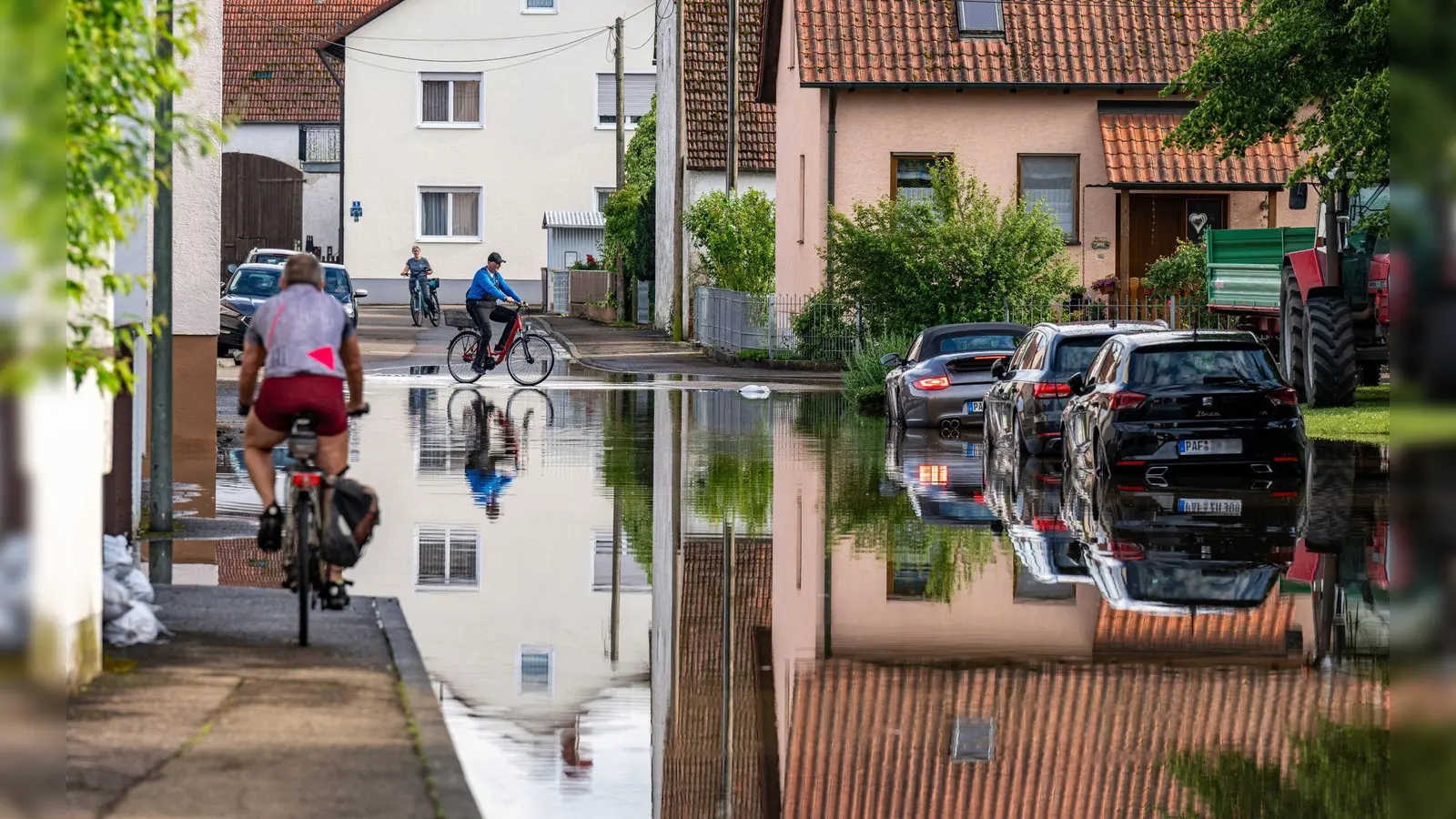 Radler fahren durch eine überflutete Straße. Im Bereich der Gemeinde Baar-Ebenhausen war ein Damm an zwei Stellen geborsten. (Foto: Armin Weigel/dpa)