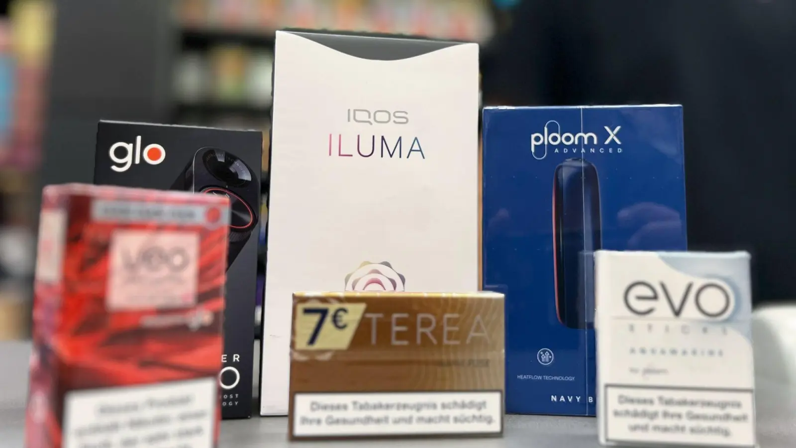 Die Tabakerhitzer-Elektrogeräte der Marken Glo von British American Tobacco (BAT), Iqos von Philip Morris und Ploom von Japan Tobacco International (JTI) mit den dazugehörigen Tabakstick-Marken liegen auf der Verkaufstheke eines Geschäfts. (Foto: Wolf von Dewitz/dpa)