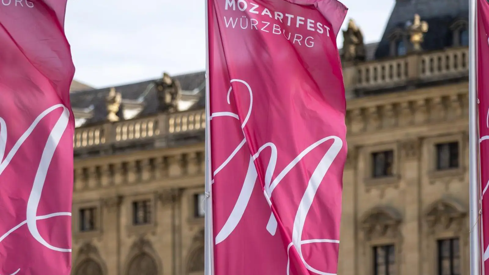 Fahnen mit der Aufschrift „Mozartfest Würzburg“ wehen vor der Würzburger Residenz. (Foto: Daniel Karmann/dpa)