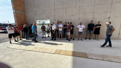 Der Bürgermeister, Stadträte und Mitglieder der Feuerwehr lauschten gemeinsam, als Gerhard Hofmann (im blauen Shirt) im gewaltigen Rohbau der neuen Fahrzeughalle über die Fortschritte beim Bau des neuen Feuerwehrhauses referierte. (Foto: Heike Gareis)