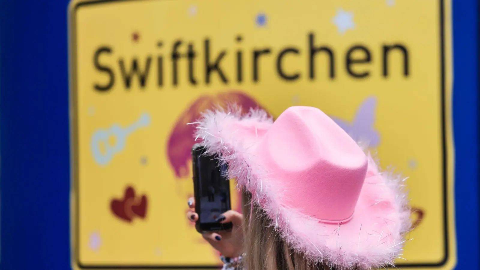 Ein Fan fotografiert vor dem Konzert der Sängerin Taylor Swift in Gelsenkirchen ein „Swiftkirchen“-Schild. Während des Konzerts am Abend zog der Datenverbrauch in den Handynetzen in der Veltins Arena kräftig an. (Foto: Oliver Berg/dpa)