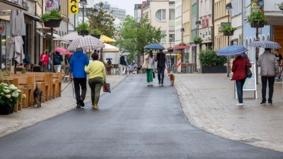 Fußgänger laufen mit Regenschirmen über die Rückertstraße. Der zu dunkle Asphalt der Straße soll nun aufgehellt werden. (Foto: Daniel Vogl/dpa)