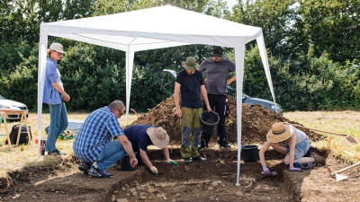 Matthias Pausch (vorne links) fachsimpelt mit den Studenten der Universität Leipzig. Um das historische Pfostenloch herum wurden Steinplatten freigelegt. Bei diesen Platten soll es sich nach Einschätzungen vor Ort lediglich um Natursteine handeln, die nicht bewusst verlegt wurden. (Foto: Tizian Gerbing)