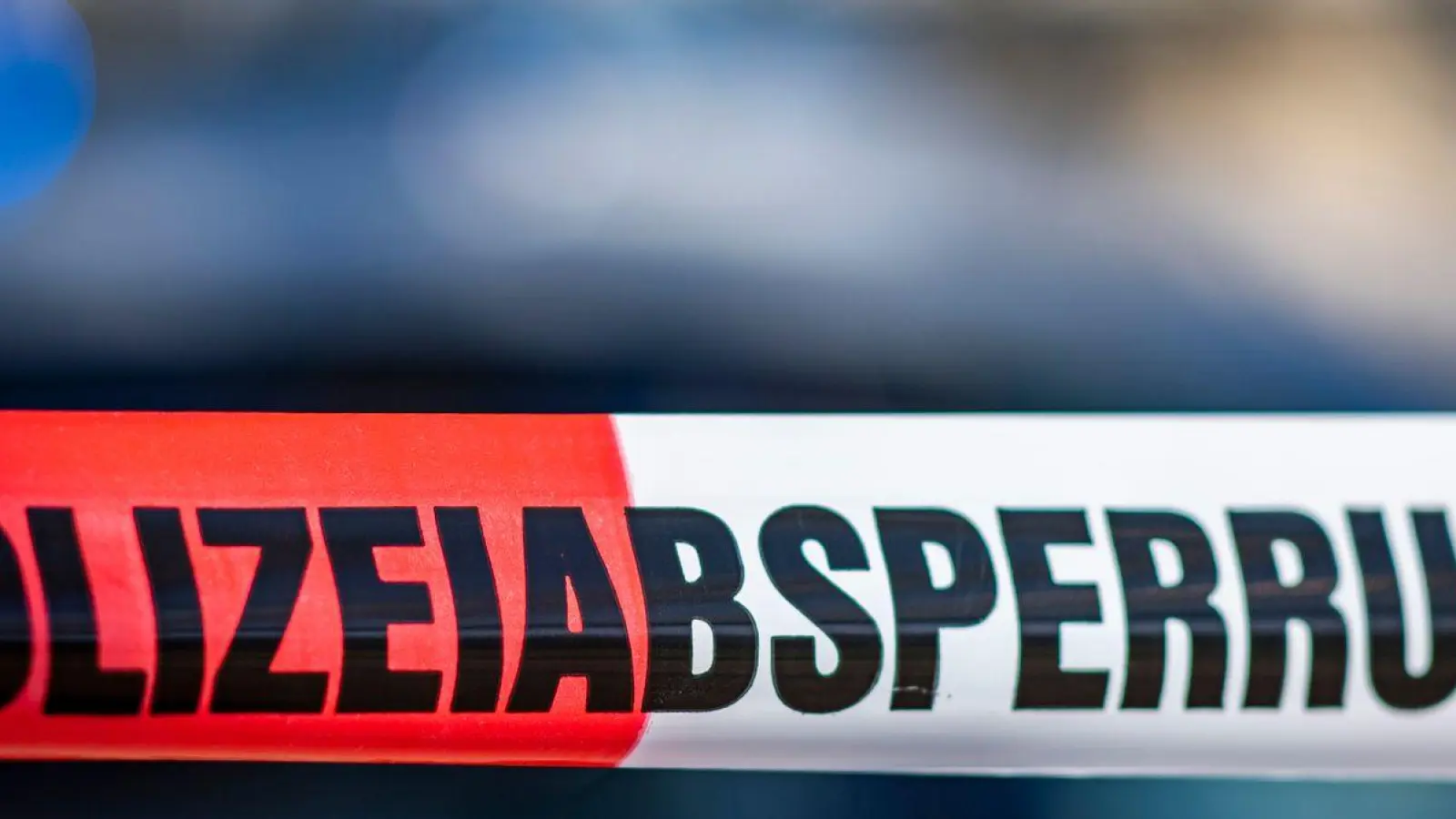 Ein Absperrband mit der Aufschrift „Polizeiabsperrung“ ist vor einem Polizeiwagen aufgespannt. (Foto: David Inderlied/dpa/Illustration)