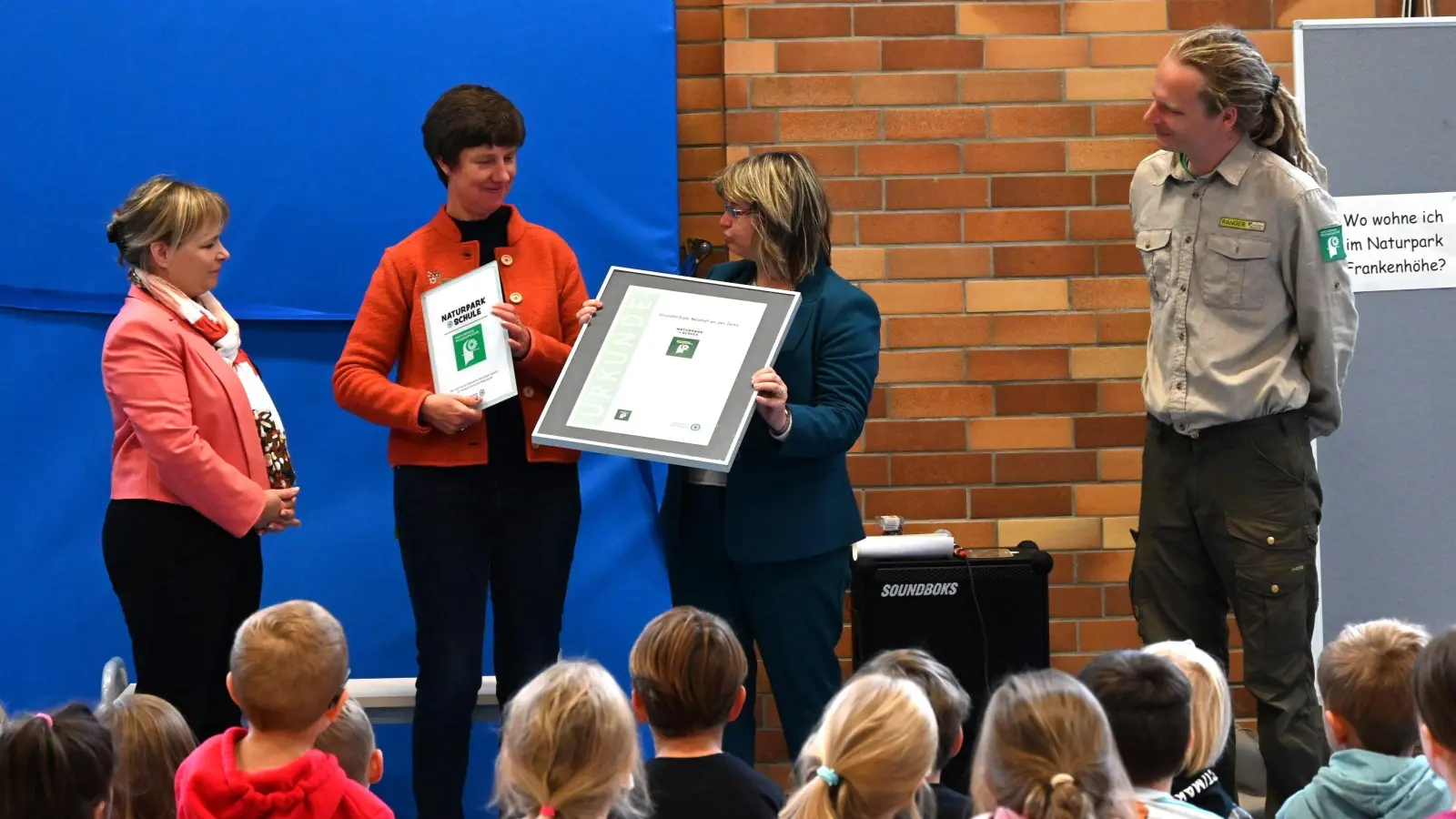 Claudia Wust, Bürgermeisterin und Vorsitzende des Schulverbands, und Schulleiterin Kerstin Stiegler bekommen von Renate Hans, der Vorsitzenden des Naturparks Frankenhöhe (von links), die Urkunde als Naturpark-Schule und ein Schild für den Eingang. Aufmerksame Beobachter sind Ranger Benjamin Krauthahn und die Kinder der Grundschule. (Foto: Manfred Blendinger)