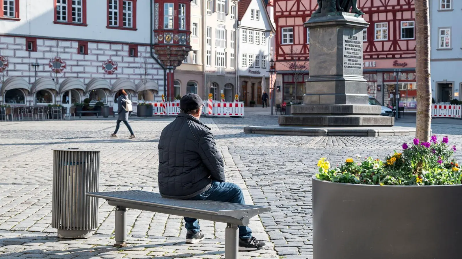 Eine Person sitzt auf dem Marktplatz in Coburg auf einer Bank in der Sonne. (Foto: Daniel Vogl/dpa)