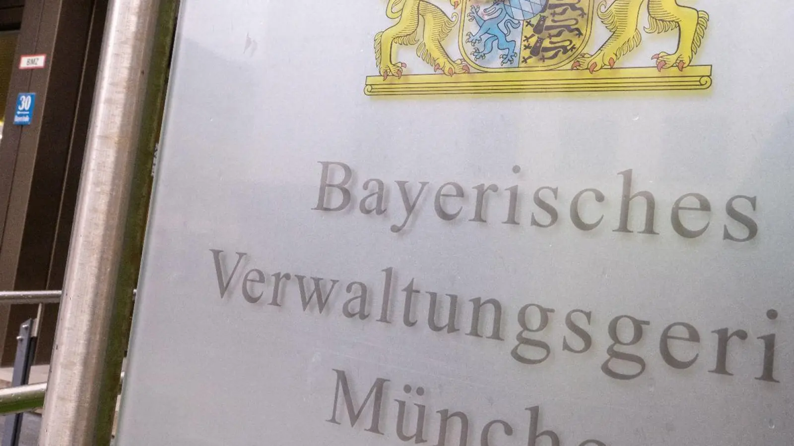 Ein Schild mit dem bayerischen Wappen und der Aufschrift „Bayerisches Verwaltungsgericht München“ hängt am Eingang des Gebäudes. (Foto: Peter Kneffel/dpa)