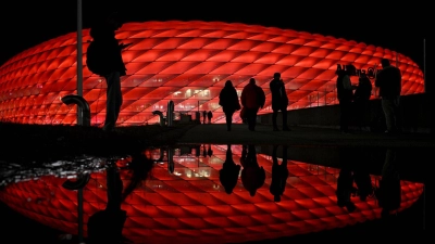 Vor dem Spiel von Bayern München gegen Paris Saint-Germain kommen Zuschauer an der Arena an, die im Dunkeln rot beleuchtet wird. (Foto: Sven Hoppe/dpa)