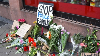 Blumen, Kerzen und Schilder liegen in Mannheim an dem Ort, an dem ein Mann Anfang Mai 2022 nach einer Polizeikontrolle starb. (Foto: René Priebe/PR-Video /dpa)