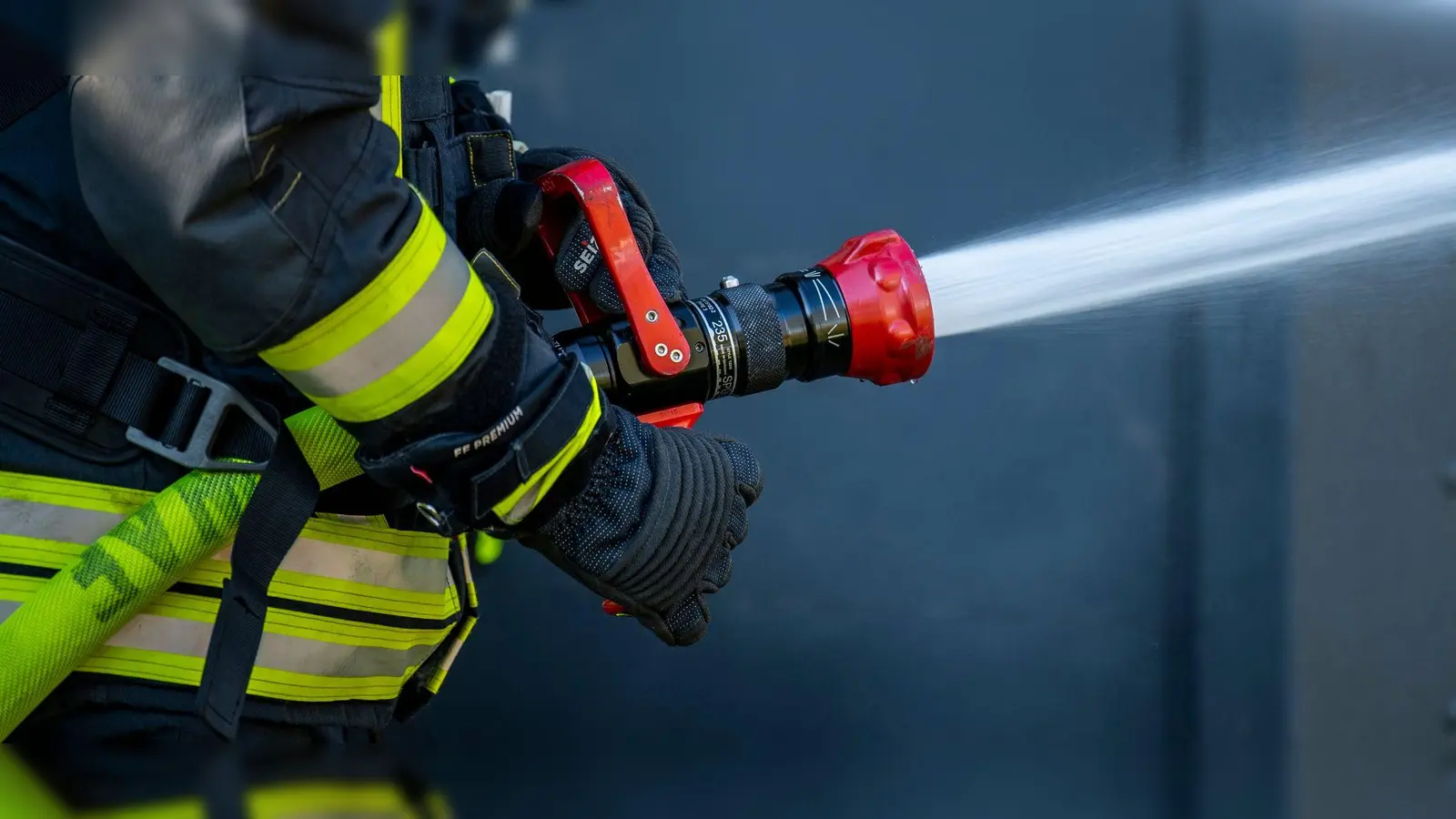 Ein Mitglied der Feuerwehr spritzt aus einem Schlauch mit Wasser. (Foto: David Inderlied/dpa/Symbolbild)