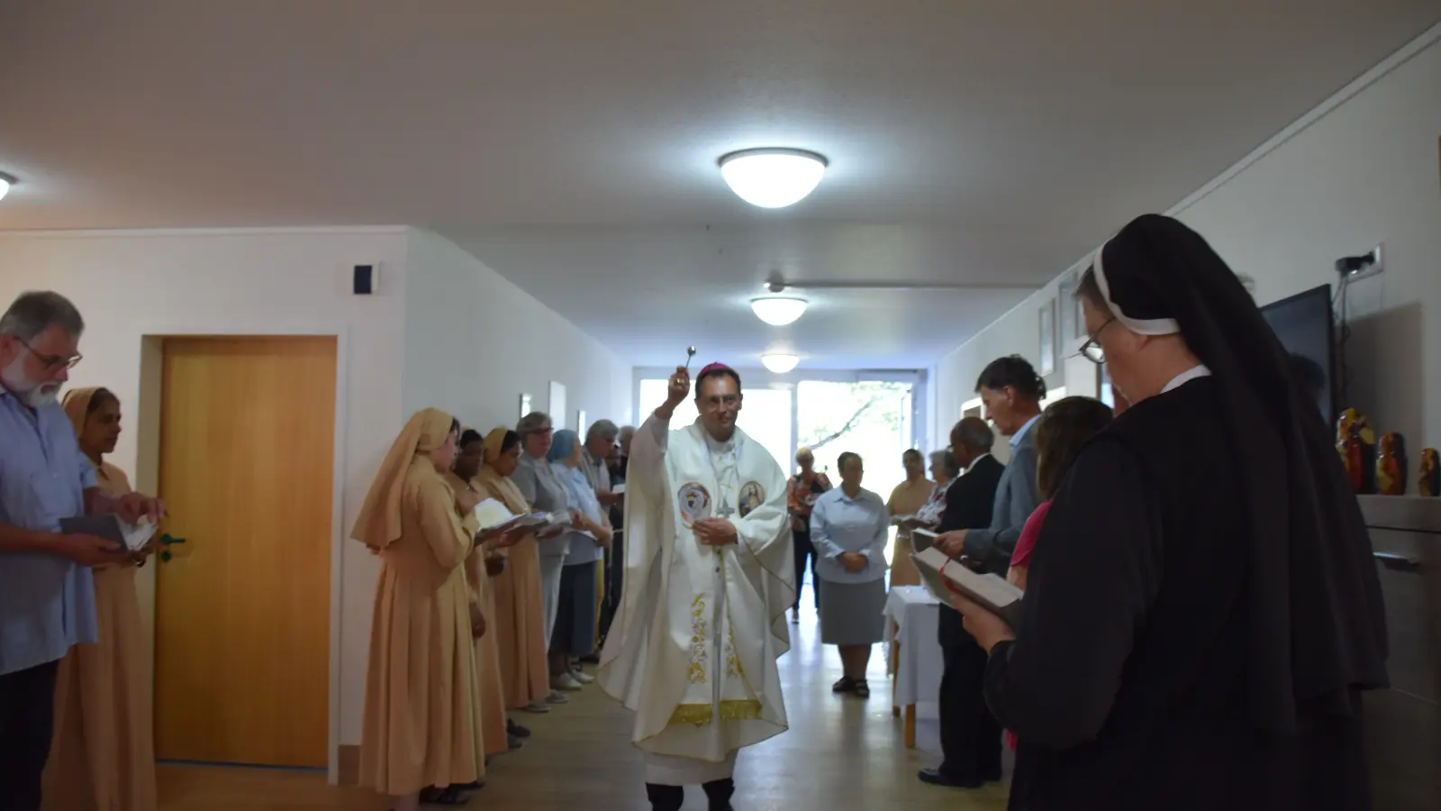 Erzbischof Herwig Gössl versprengt Weihwasser in den neuen Räumen des neuen Konvents für die im korallfarbenen Gewand gekleideten „Töchter des Heiligen Herzens Jesu“-Schwestern. (Foto: Andreas Reum)