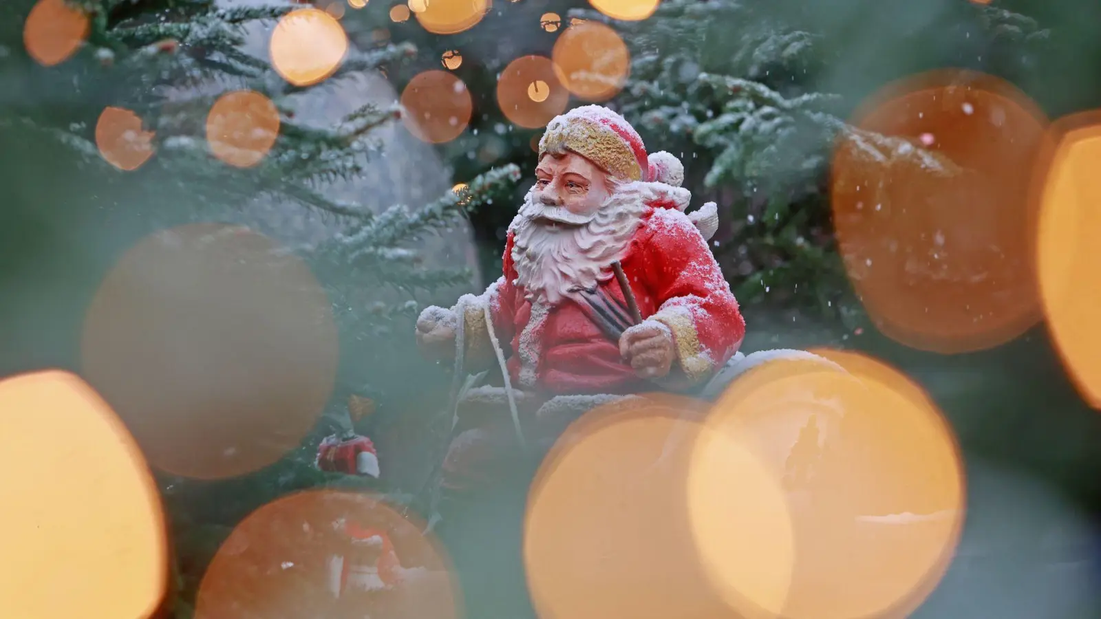 Weihnachtliches in Sachsen-Anhalt: Blick durch eine Lichterkette auf eine schneebedeckte Weihnachtsmannfigur. (Foto: Matthias Bein/dpa)