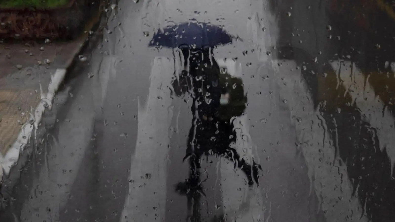 Eine Frau mit Regenschirm überquert eine Straße in Athen. (Foto: Petros Giannakouris/AP/dpa)