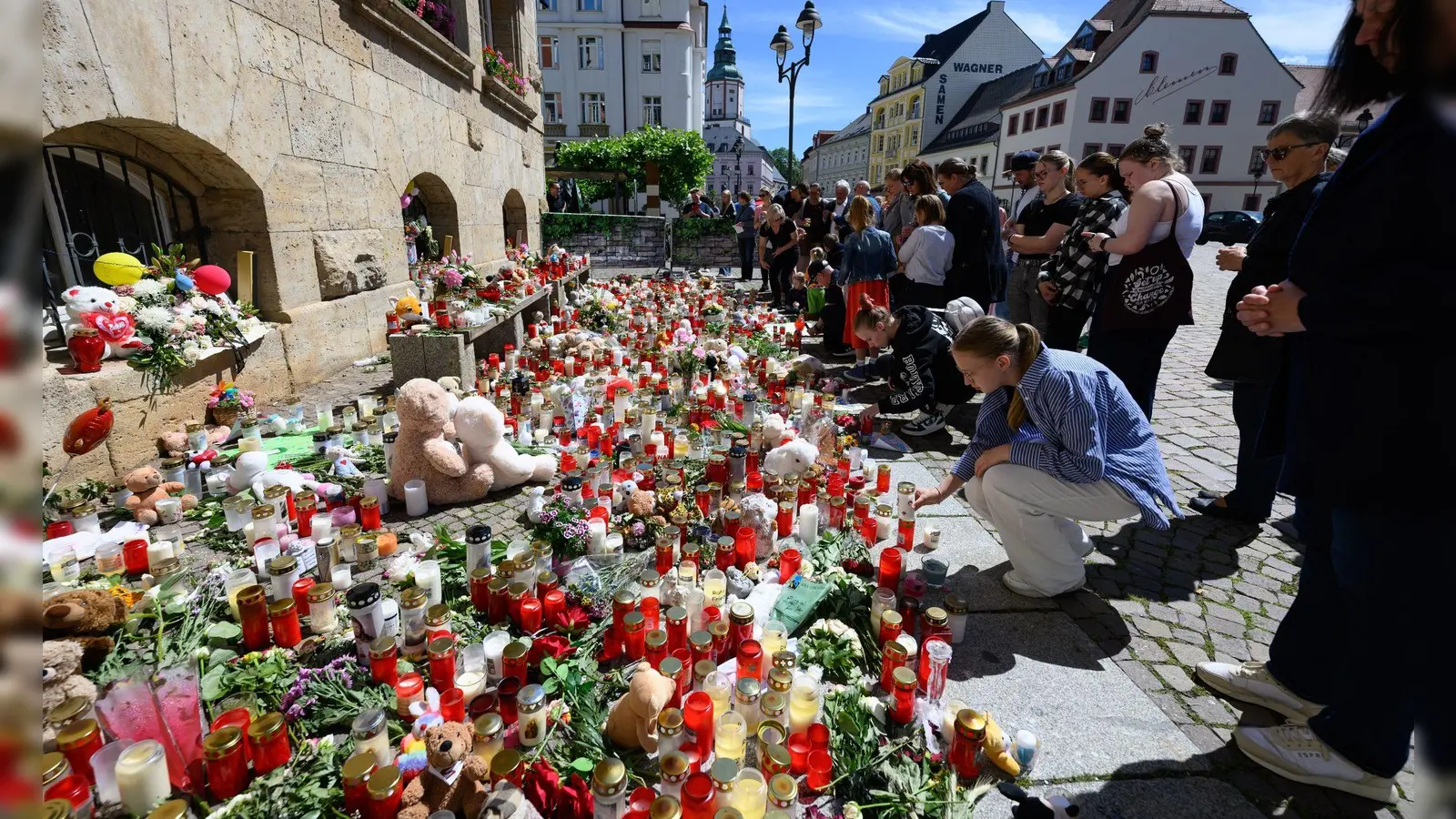 Menschen stehen am Rande eines Gottesdienstes für die getötete Valeriia in Döbeln vor Blumen und Kerzen. (Foto: Robert Michael/dpa)
