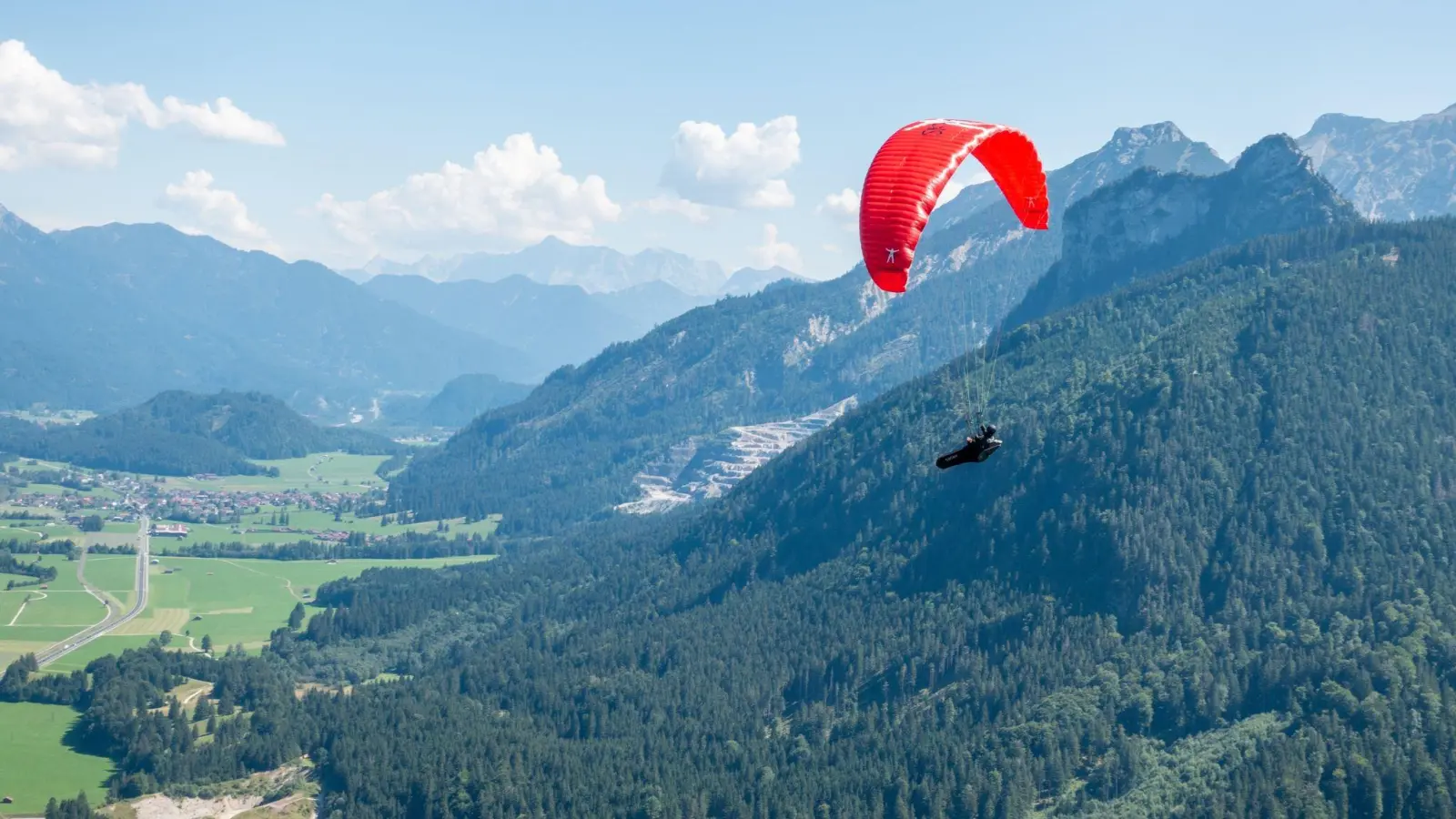 Verkehr am Himmel über Pfronten: Ein Solo-Paraglider fliegt neben dem Autoren und seinem Tandempiloten in Richtung Tal. (Foto: Andreas Drouve/dpa-tmn)