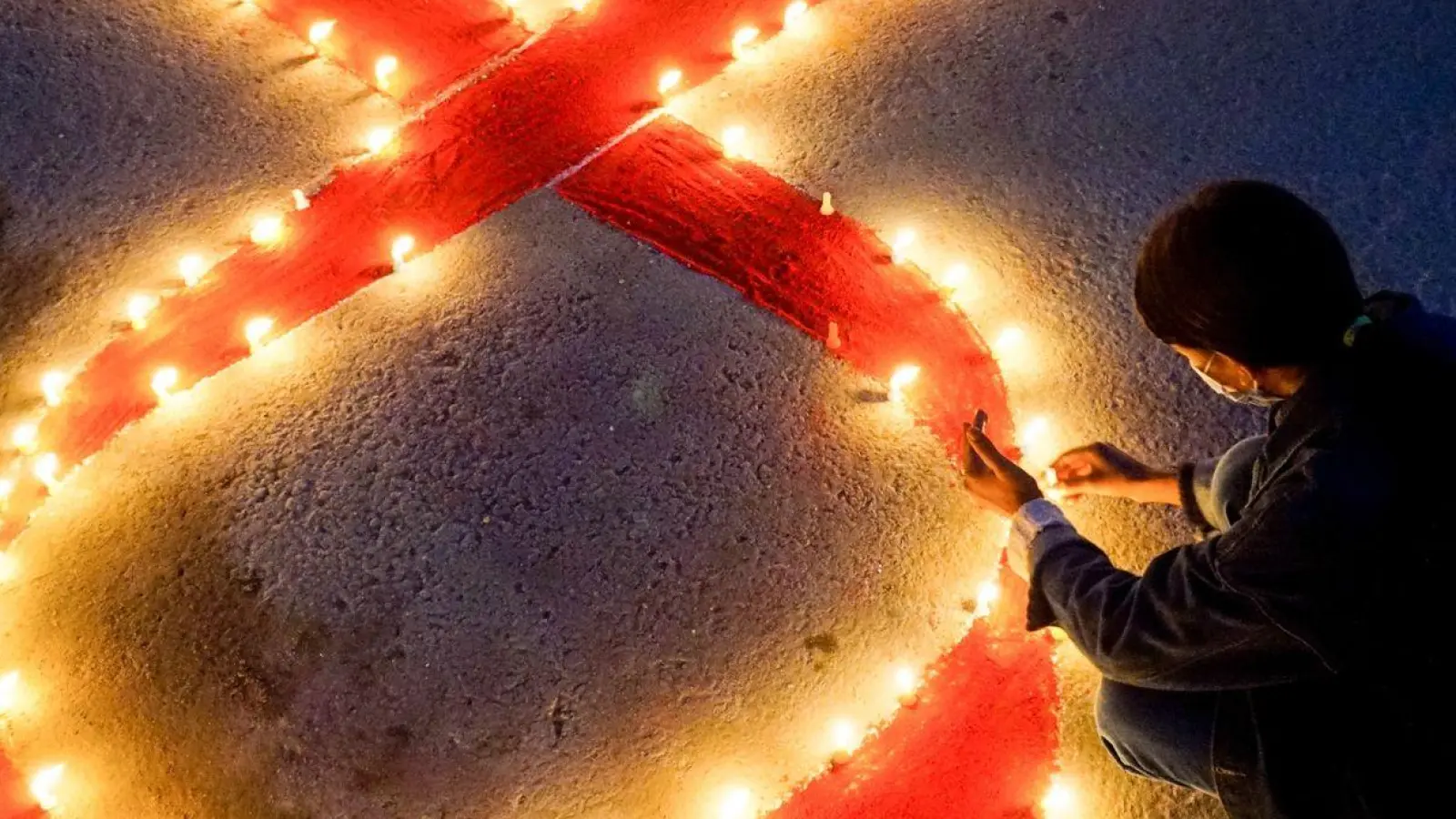 Eine Frau stellt Kerzen auf, die eine rote Schleife formen - ein weltweit anerkanntes Symbol für die Solidarität mit HIV-Infizierten. (Foto: Sunil Pradhan/SOPA Images via ZUMA Wire/dpa)