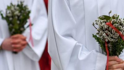 Ministranten gehen bei der Palmprozession am Palmsonntag durch die Innenstadt von Bad Tölz und tragen Palmbuschen in den Händen. (Foto: Tobias Hase/dpa)