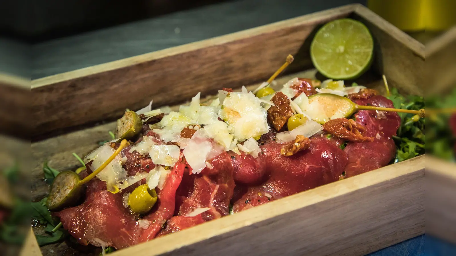 Statt auf dem runden Teller wird das Carpaccio im „The Dry Gin and Beef Club“ auf einem kleinen Tablett auf Rucola angerichtet. Limette träufelt der Gast zum Schluss selbst darüber.  (Foto: Christin Klose/dpa-tmn)