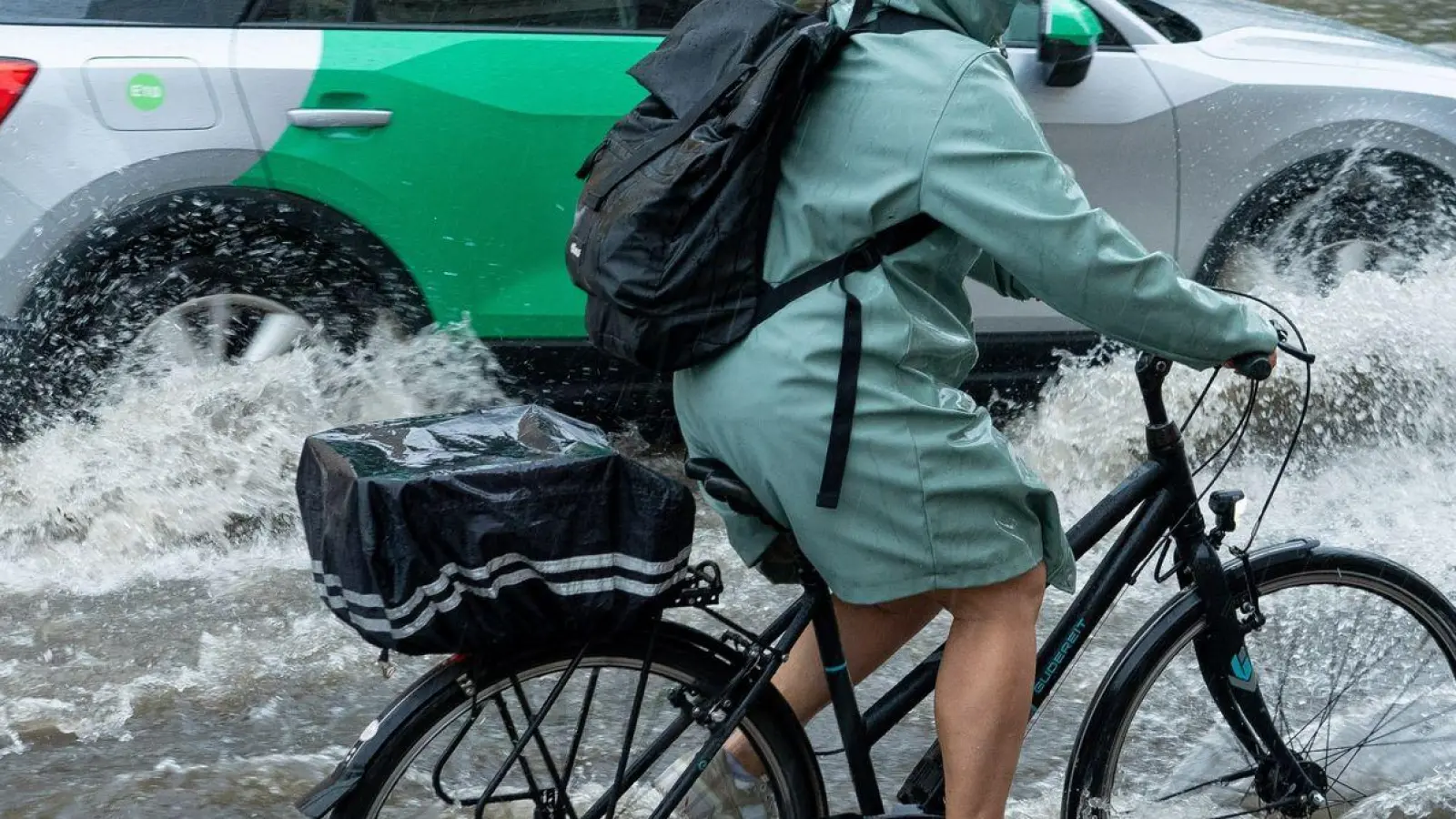 Eine Radfahrerin und ein Auto fahren im Schritttempo durch die überflutete Zeppelinstraße. (Foto: Georg Moritz/dpa)