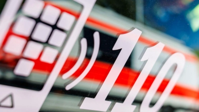 Die Nummer des Polizeinotrufs 110 steht auf der Scheibe eines Polizeifahrzeugs, in der sich ein Fahrzeug vom Roten Kreuz spiegelt. (Foto: Daniel Karmann/dpa)
