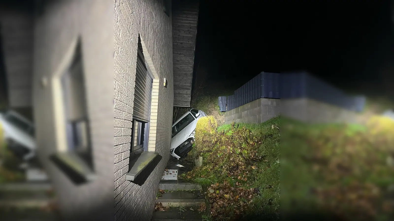 Das Auto steckt zwischen einem Abhang und dem verklinkerten Wohnhaus fest. (Foto: -/Kreispolizei Paderborn/dpa)