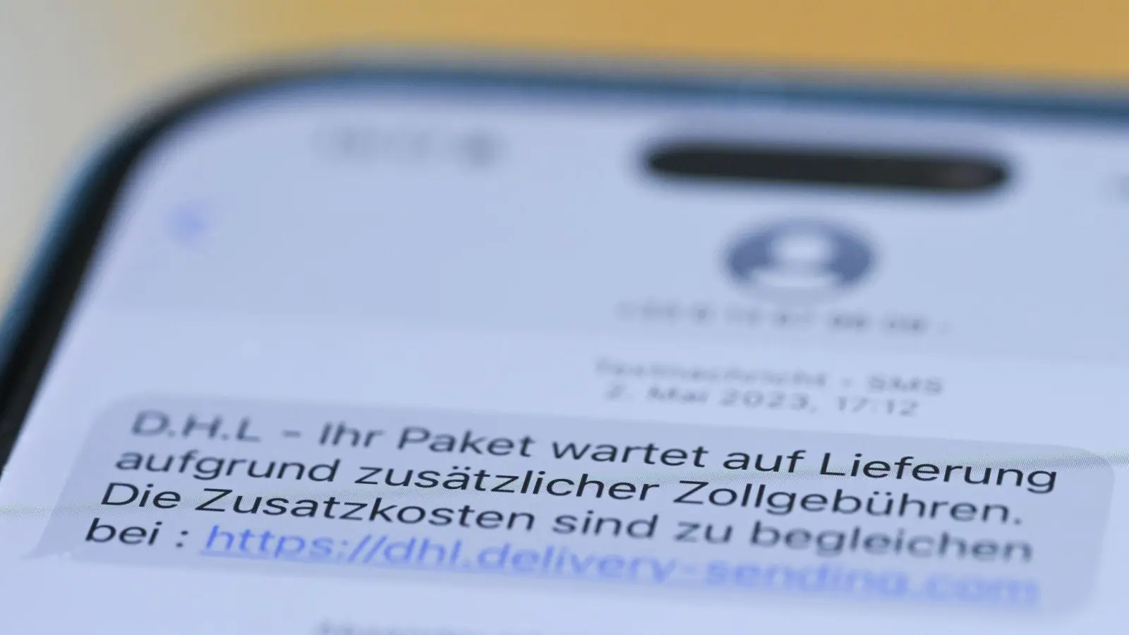 Auf einem Smartphone ist eine Betrugs-SMS zu lesen, in der Kriminelle ein Paket ankündigen und dafür Zollgebühren einfordern.  (Foto: Wolf von Dewitz/dpa)