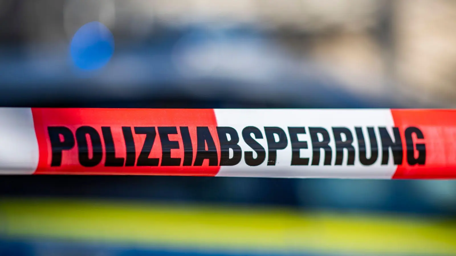 Ein Absperrband mit der Aufschrift „Polizeiabsperrung“ ist vor einem Polizeiwagen aufgespannt. (Foto: David Inderlied/dpa)