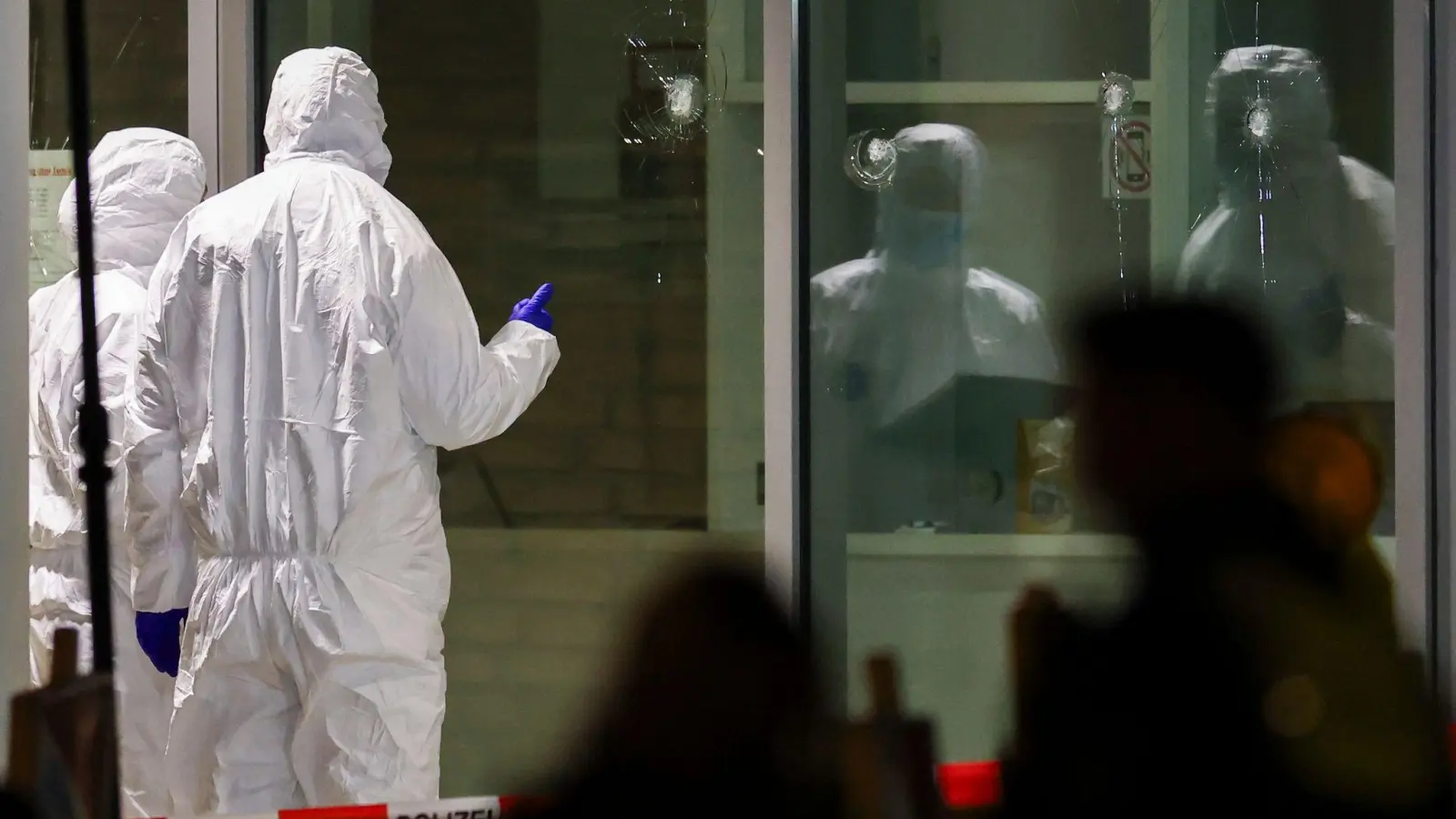 Polizeibeamte der Spurensicherung in weißen Schutzanzügen untersuchen Löcher in Glasscheiben des Kinos. (Foto: Christoph Reichwein/dpa)