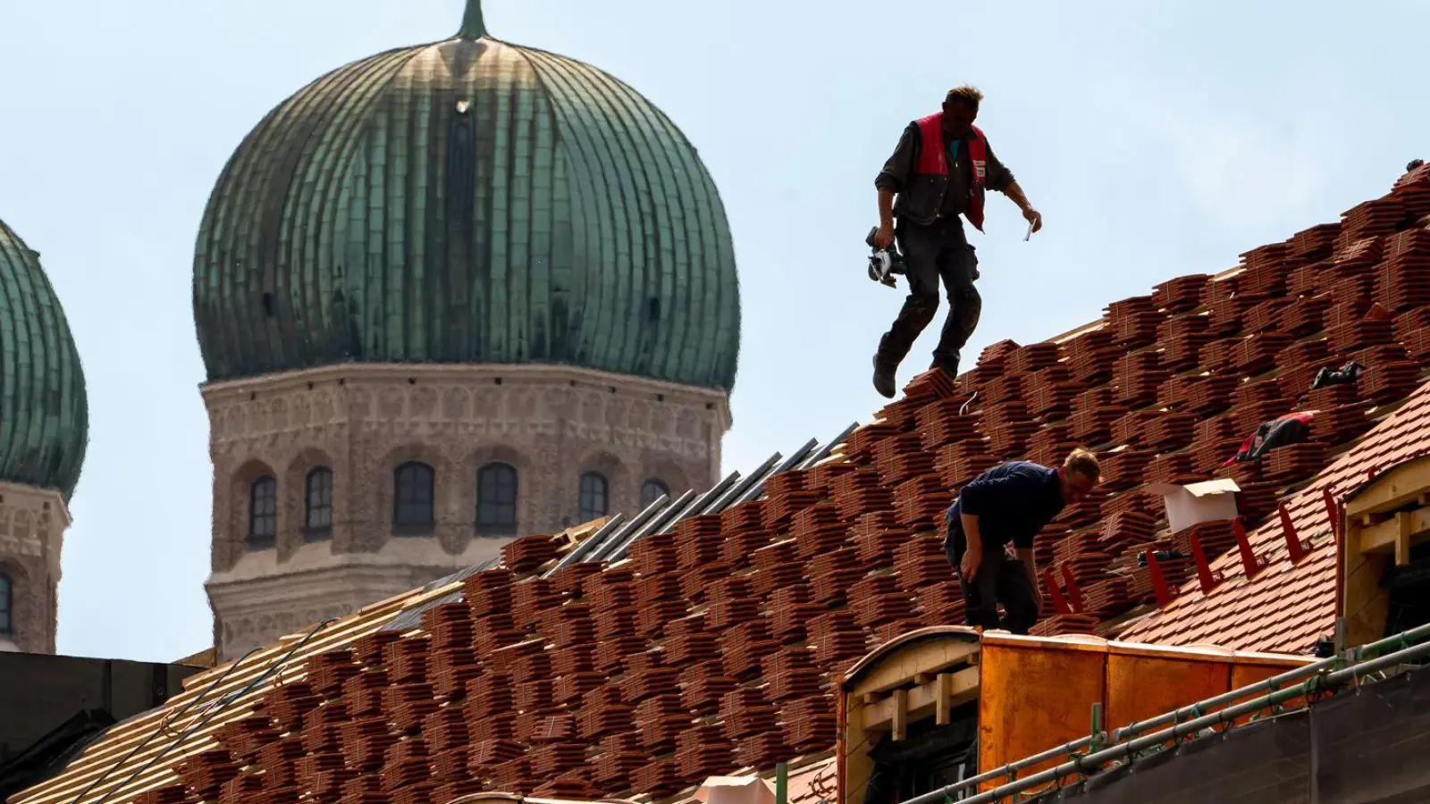 Dachdecker auf einem Hausdach vor der Kulisse der Münchner Frauenkirche (Foto: Peter Kneffel/dpa)