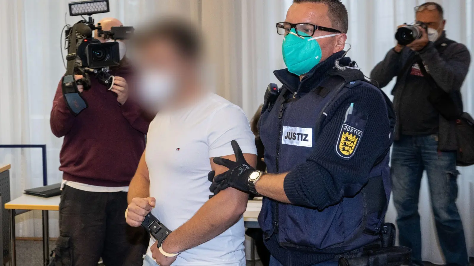 Im Landgericht führt ein Justizbeamter einen Mann an Journalisten vorbei in den Sitzungssaal. (Foto: Stefan Puchner/dpa)