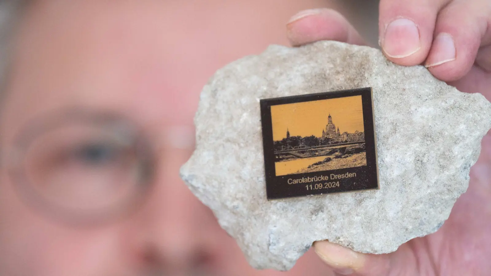 Torsten Daae, Geschäftsführer im Dresdner Laden „Catapult“, hält einen Stein des abgerissenen Brückenteils der eingestürzten Carolabrücke mit einer Plakette in der Hand. (Foto: Sebastian Kahnert/dpa)